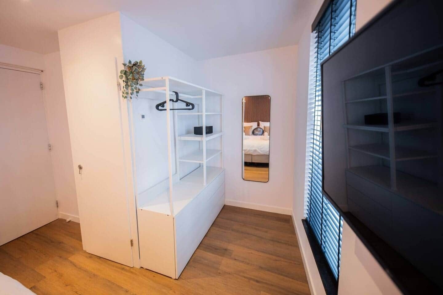 A compact room with a built-in wardrobe, a mirror, and a window with blinds.