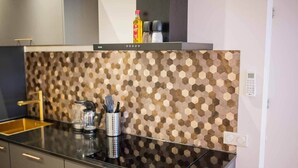 A modern kitchen with a black countertop, a hexagonal patterned backsplash, and stainless steel appliances. - Luxurious 35m² Designer Studio (R-51-A) (Eindhoven)