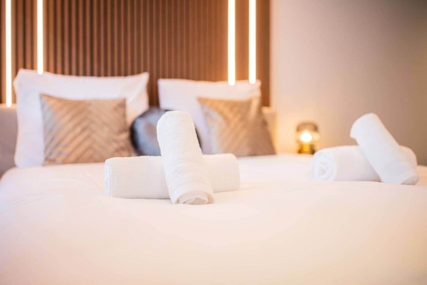 A neatly made bed with rolled white towels and a bedside lamp.