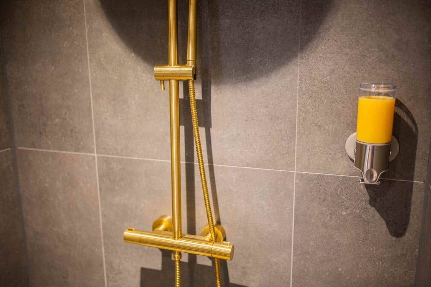 Una ducha con una manguera dorada y un vaso de jugo de naranja sobre una pared.