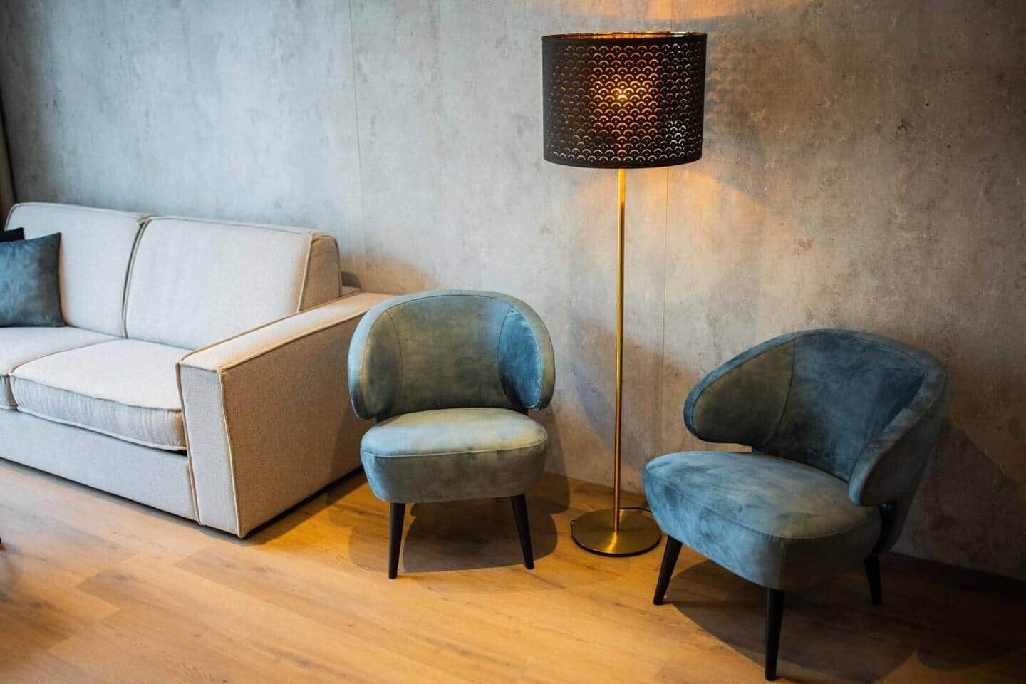 Une pièce avec un canapé blanc, deux fauteuils bleus et un lampadaire.