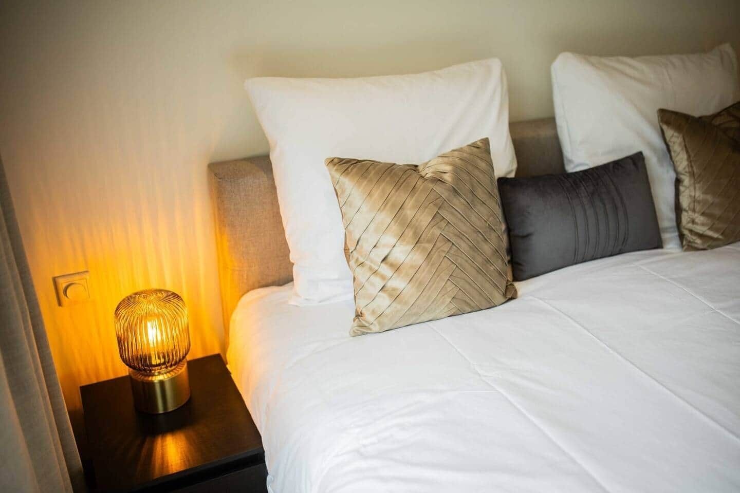 Een hotelkamer met een bed, een nachtkastje met een lamp en een wandlamp.