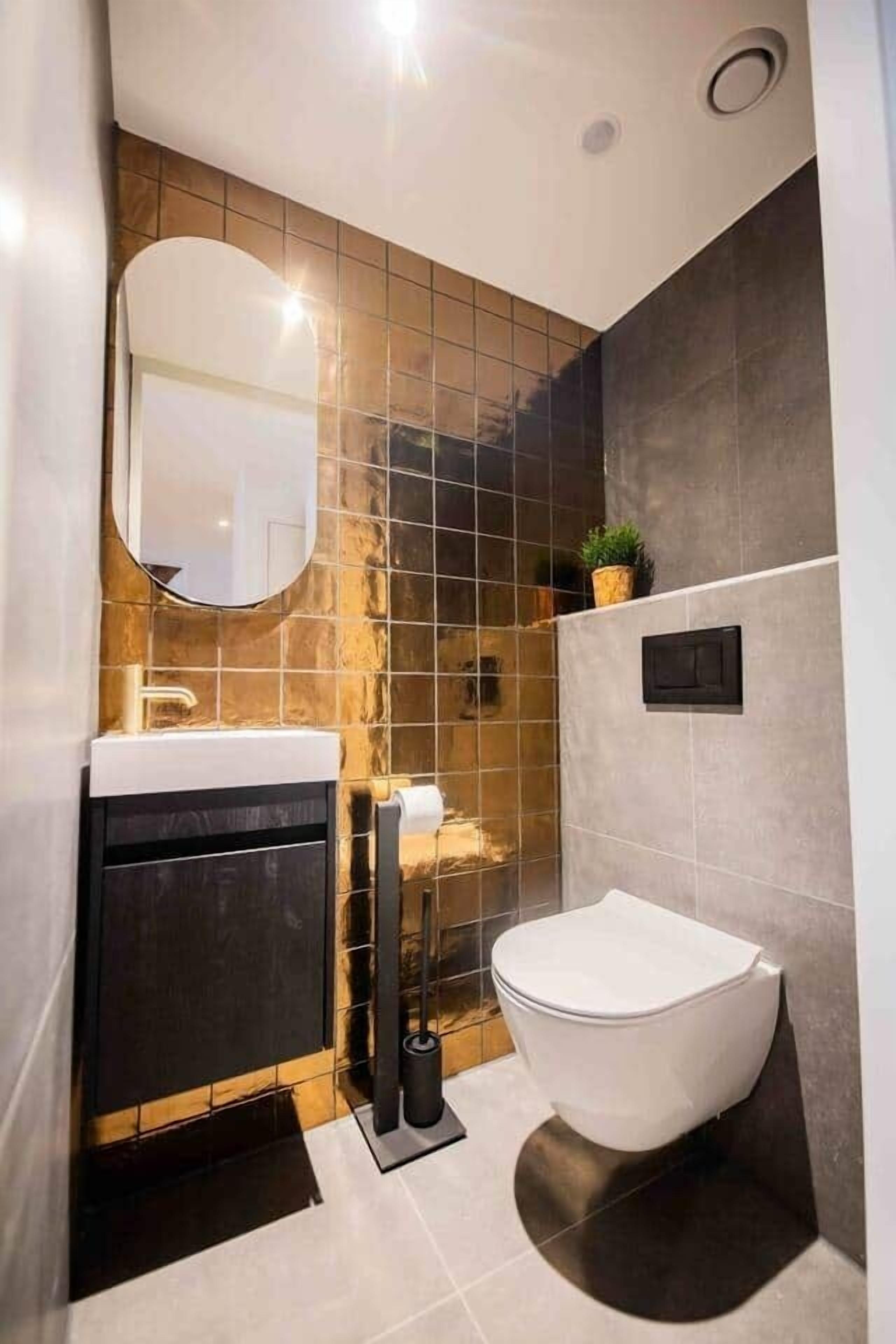 Un baño moderno con un lavamanos blanco, un espejo redondo y un inodoro.
