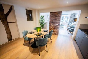 Un coin repas comprenant une table ronde, quatre chaises, une plante en pot et un mur décoratif en pierre.