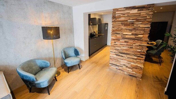A modern living room with two blue armchairs, a floor lamp, a kitchen area, and a wooden accent wall. - Historical City Retreat with Sauna option (R-51-B) (Eindhoven)