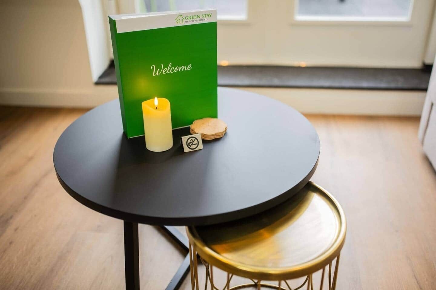 Eine grüne Willkommenskarte mit einer Kerze und einem Rauchverbot-Schild auf einem kleinen runden Tisch.