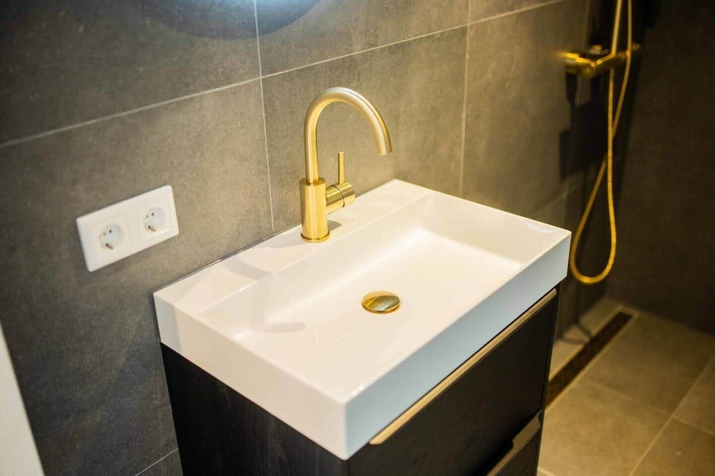 Baño con lavamanos blanco, grifo dorado y manguera de ducha.