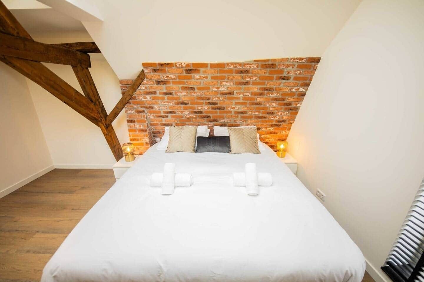 A bedroom with a brick-patterned headboard, a neatly made bed with white linens, and two bedside lamps.