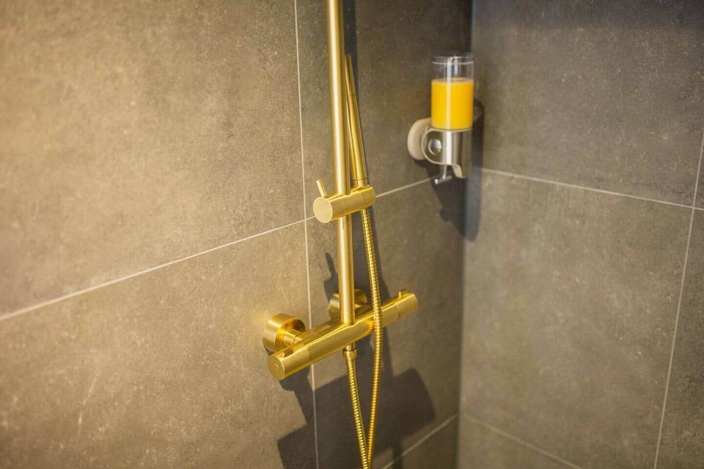 Ducha con una manguera dorada y un dispensador de jabón en la pared.