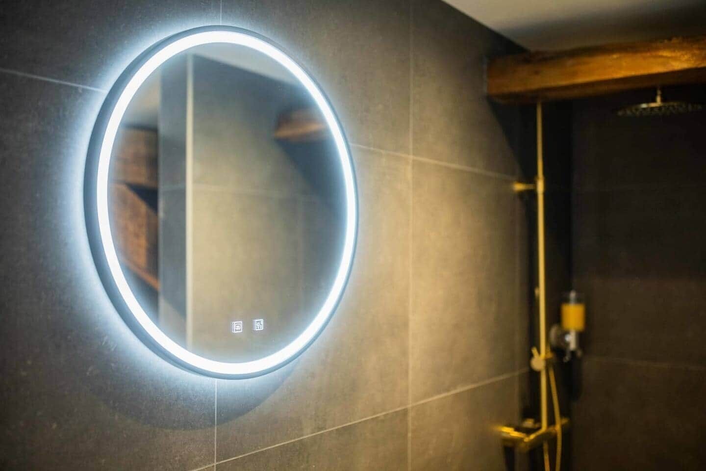 A bathroom with a circular mirror, a shower, and a wall-mounted light fixture.