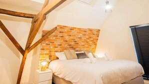 A bedroom with exposed wooden beams, a brick accent wall, a bed, bedside tables, and a hanging light fixture. - Spectacular 70m² Penthouse with Terrace (R-51-C) (Eindhoven)