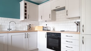 Una cocina moderna con armarios blancos, un horno Bosch, una tetera, un tostador y una encimera de madera.