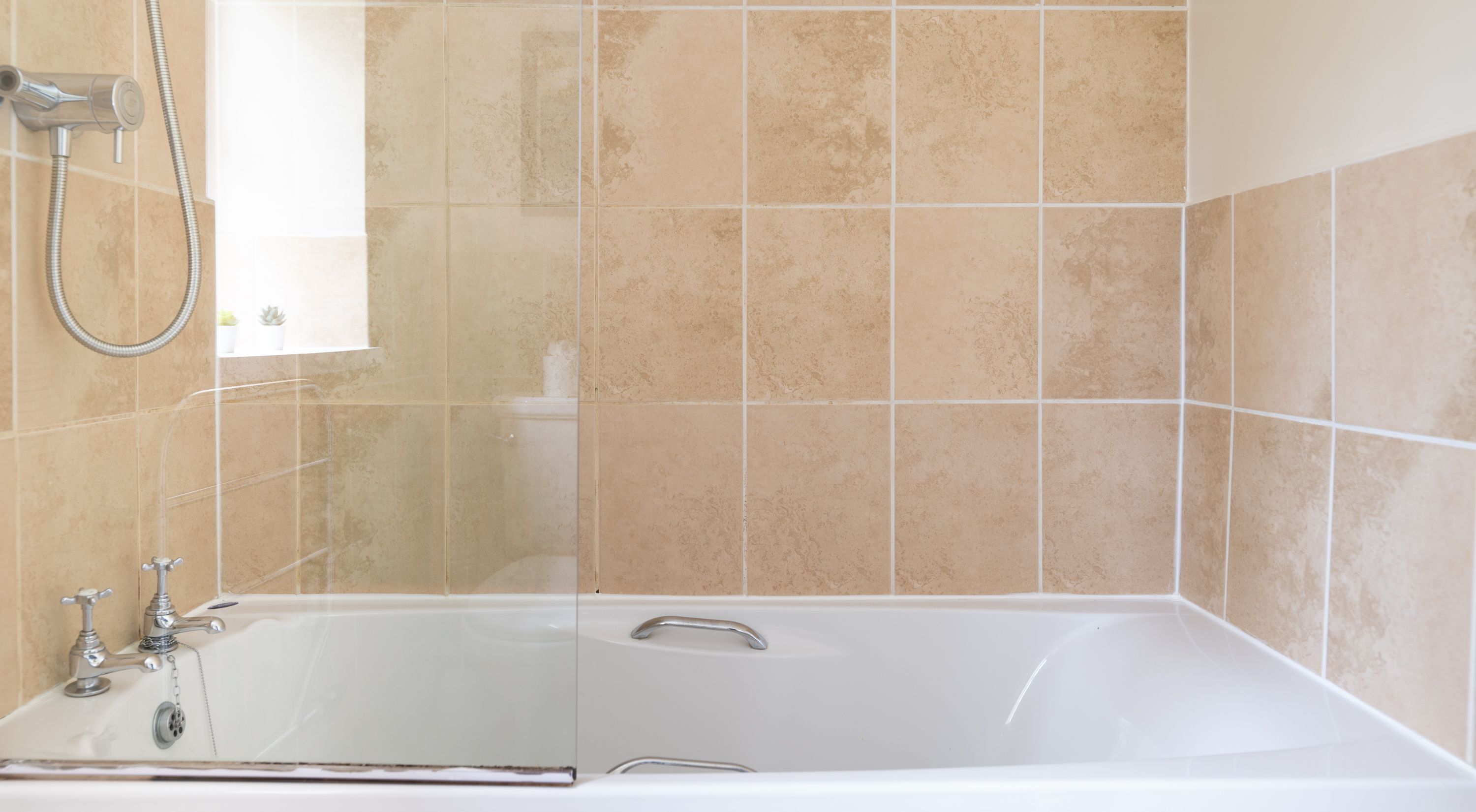 Ein Badezimmer mit Badewanne, Dusche und beige gefliesten Wänden.