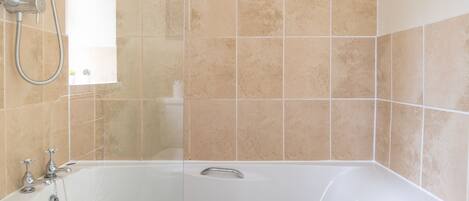 Ein Badezimmer mit Badewanne, Dusche und beige gefliesten Wänden.