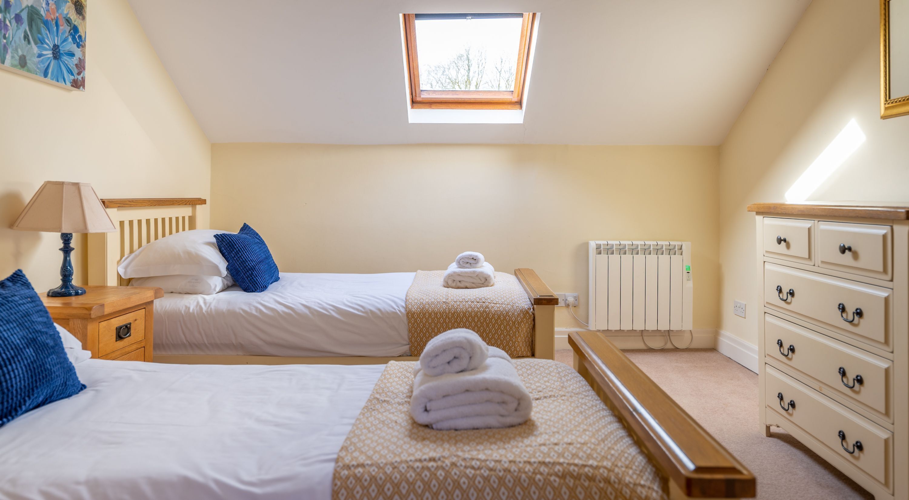 A bedroom with two beds, a nightstand, a dresser, a radiator, and a skylight.