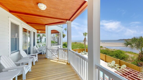 A wooden deck with white chairs and a view of the beach.
