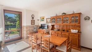 Uma sala de jantar com mesa e cadeiras de madeira, cozinha com armários de madeira e uma porta de vidro deslizante que dá para um alpendre.
