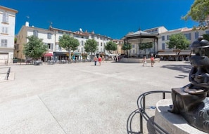 Ein öffentlicher Platz mit Gebäuden, einer Statue und Außenbereichs-Sitzgelegenheiten.