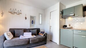 A modern living room with a grey sofa, a small coffee table, and a kitchen area with teal cabinets and a stove. - (058) Le petit National (Antibes)