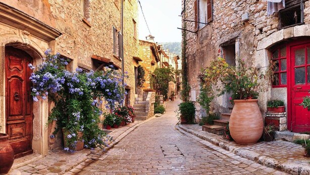 A narrow cobblestone street lined with stone buildings, featuring a red door and a large terracotta pot on the right. - (058) Le petit National (Antibes)