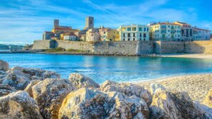 A coastal town with buildings along a stone wall by the sea. - (058) Le petit National (Antibes)