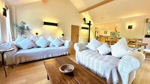 Een ruime woonkamer met twee witte banken, een houten salontafel en een eethoek op de achtergrond.