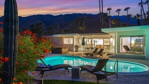 Un espace piscine avec des chaises longues, un jacuzzi et une maison moderne dotée de grandes fenêtres.