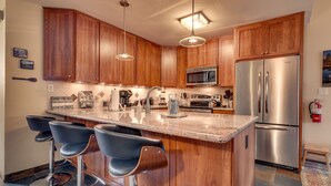 A modern kitchen with wooden cabinets, stainless steel appliances, and a bar area with stools. - Livin' Lodge: 3  BR, 2  BA Townhouse in Carnelian Bay, Sleeps 8 (Carnelian Bay)