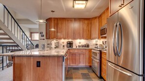 A modern kitchen with wooden cabinets, stainless steel appliances, a central island, and a staircase leading to another level. - Livin' Lodge: 3  BR, 2  BA Townhouse in Carnelian Bay, Sleeps 8 (Carnelian Bay)
