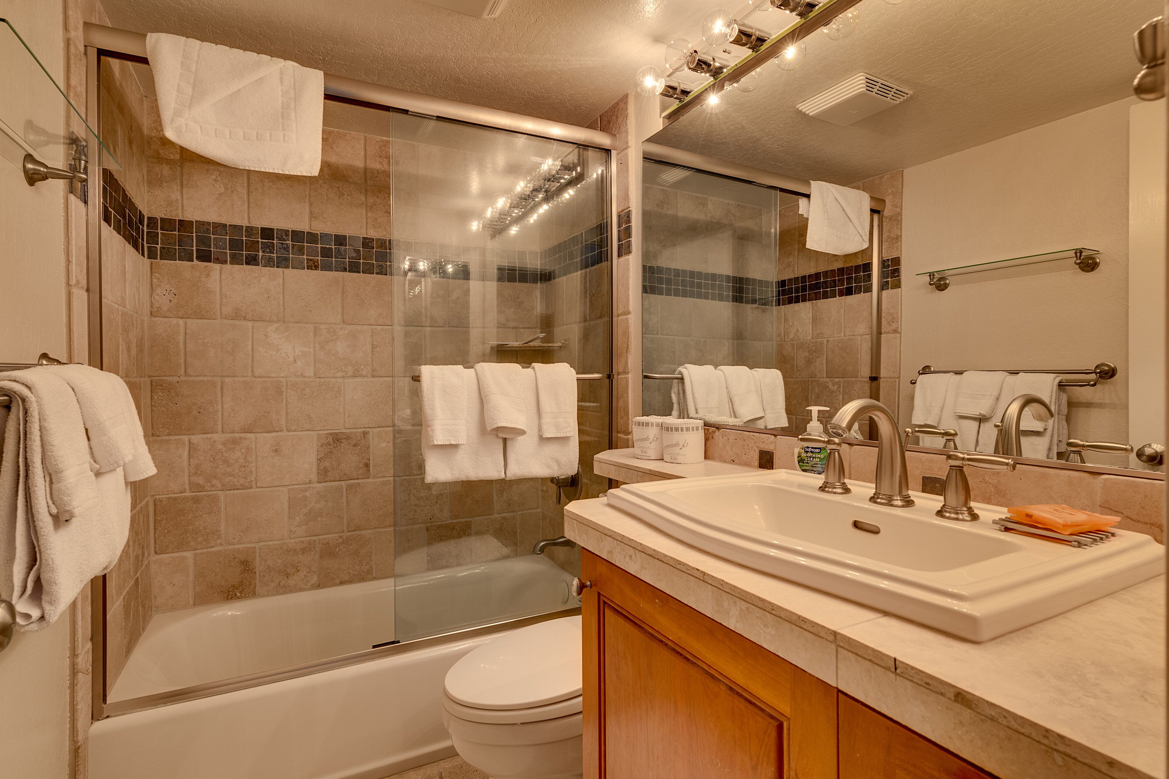 A modern bathroom with a glass-enclosed shower, a bathtub, a toilet, and a vanity with a sink and mirror.