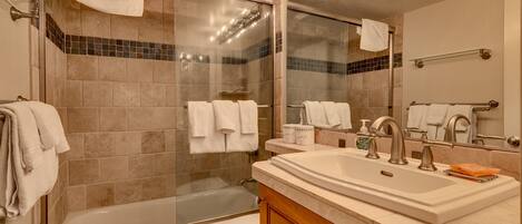 A modern bathroom with a glass-enclosed shower, a bathtub, a toilet, and a vanity with a sink and mirror.