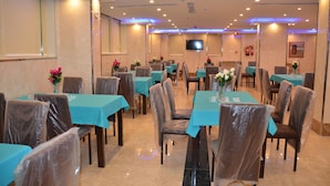 Un comedor de hotel con mesas cubiertas de manteles azules, sillas envueltas en plástico y centros de mesa florales.