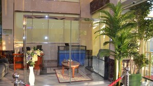 Zona de recepción con separador de vidrio, mostrador de recepción, área de espera con una mesa y sillas, y una planta en maceta.