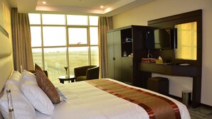 Habitación de hotel con una cama grande, un escritorio con espejo, televisión y vistas al exterior.
