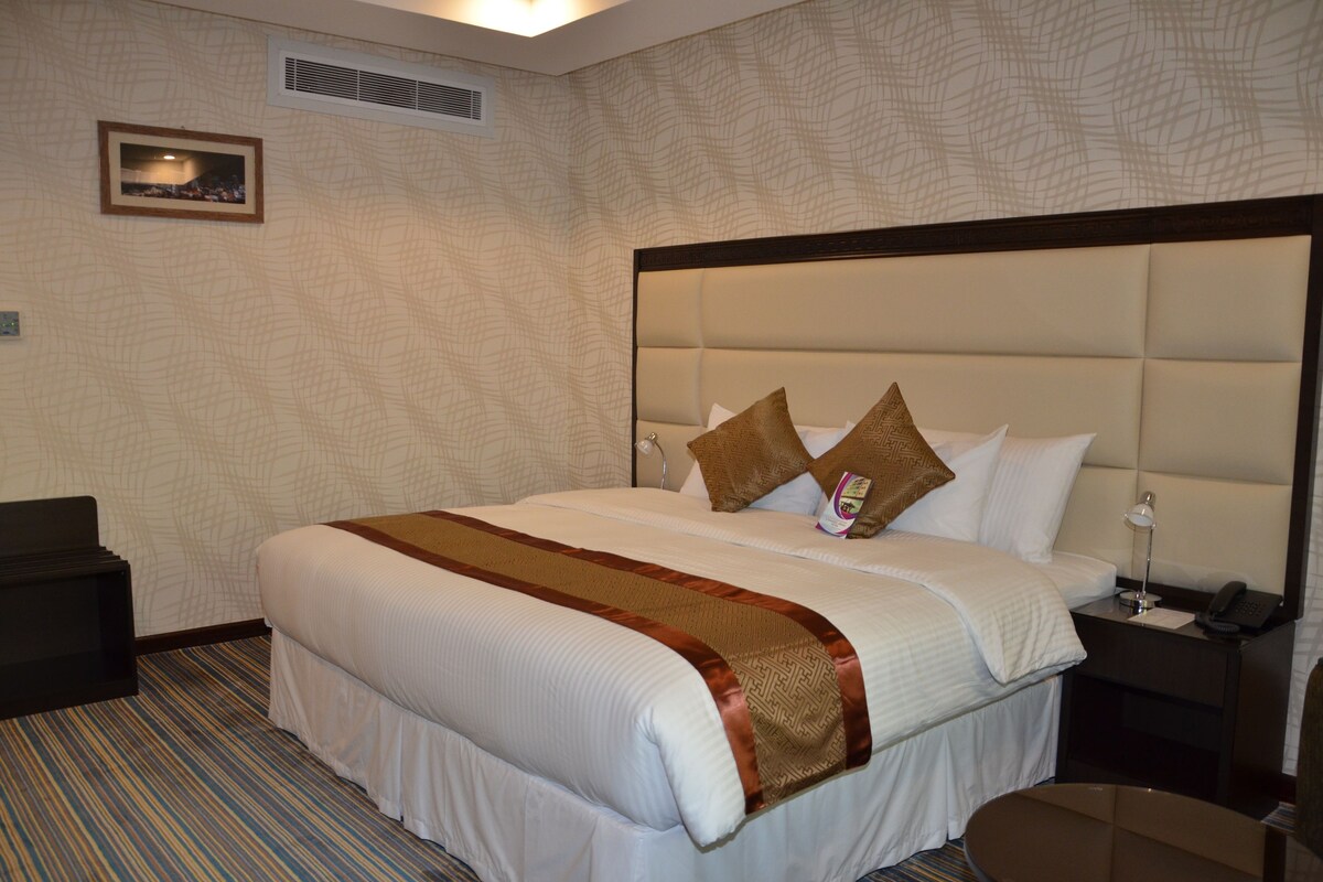 A hotel room with a large bed, a bedside table with a lamp, a telephone, and a picture on the wall.