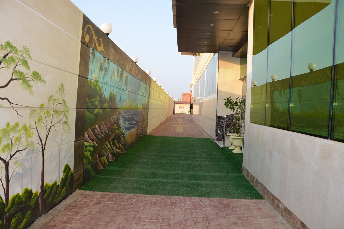 A corridor with a mural on the left wall, a green carpet, and a tiled floor.