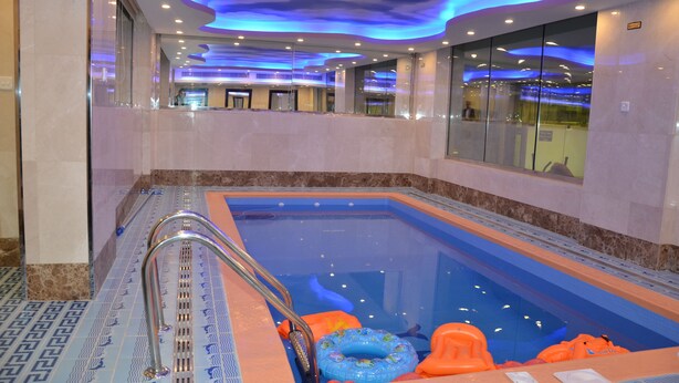 Una piscina con barrera de vidrio, flotadores azules y naranja, y una escalera de metal.