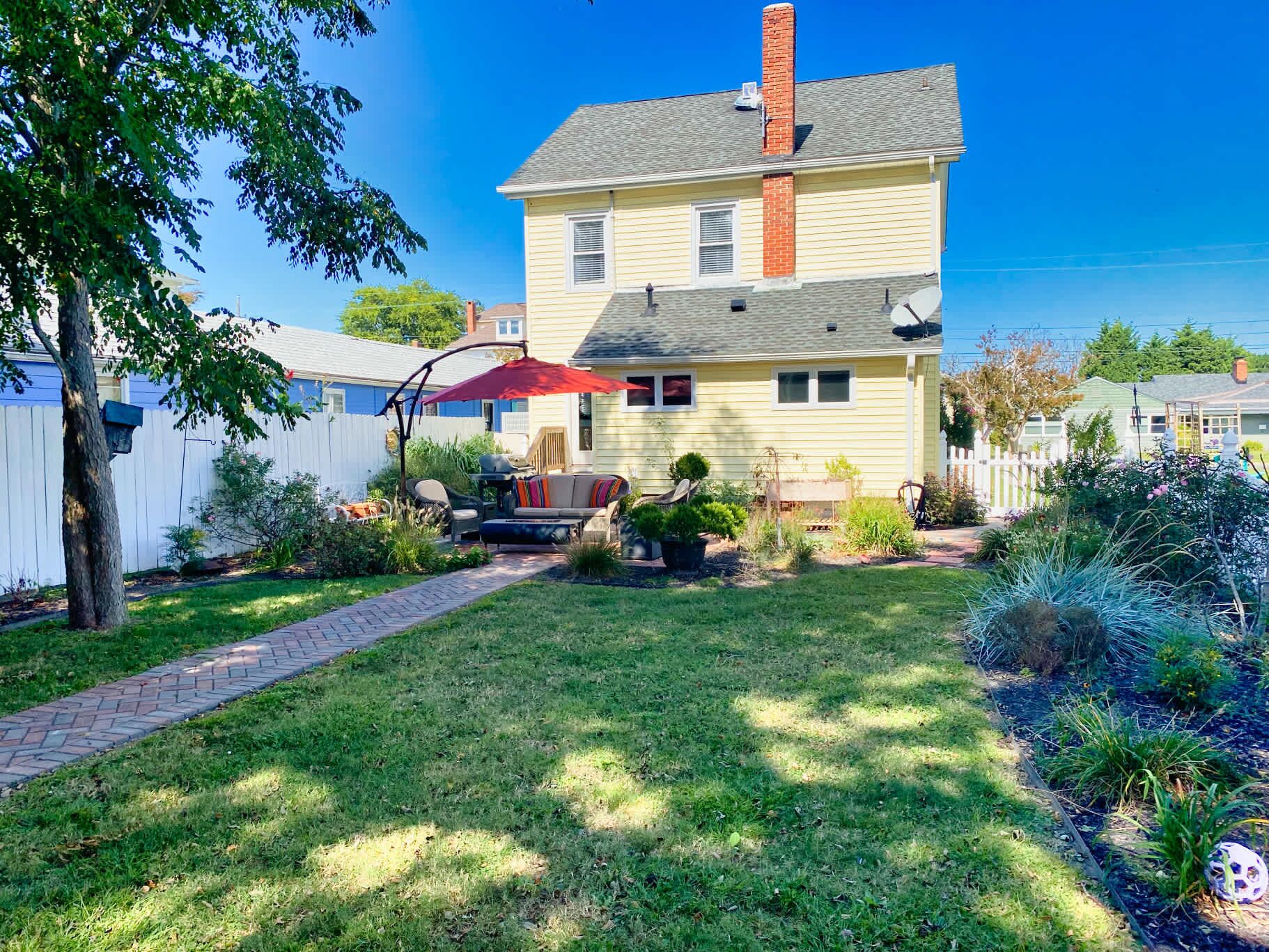 A two-story house with a front yard, a patio with outdoor furniture, and a white picket fence.