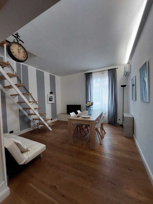 Un soggiorno moderno con una scala in legno, un'area pranzo con tavolo e sedie, e un televisore a schermo piatto.