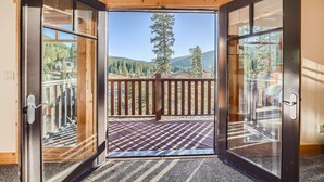 Une pièce dotée d’une grande porte-fenêtre coulissante donnant sur un balcon avec une terrasse en bois et une vue sur une zone montagneuse boisée.