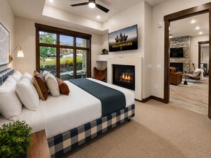 A bedroom with a large bed, a fireplace, a TV, and a view of the outdoors.
