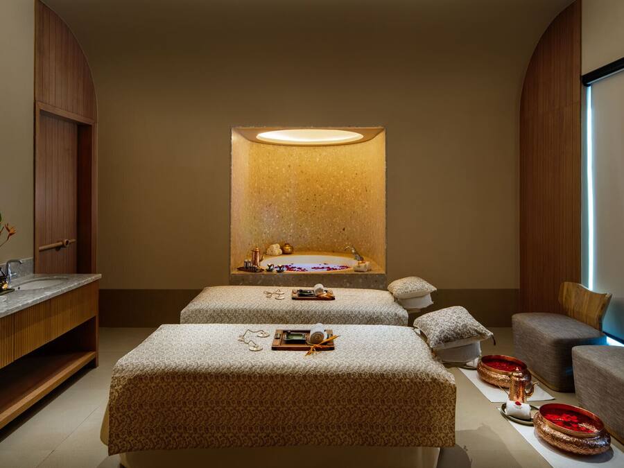 A spa room with a large mirror, a bathtub, and two massage tables.