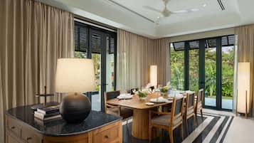 A dining area with a wooden table set for four, surrounded by chairs, with a large window offering a view of greenery.