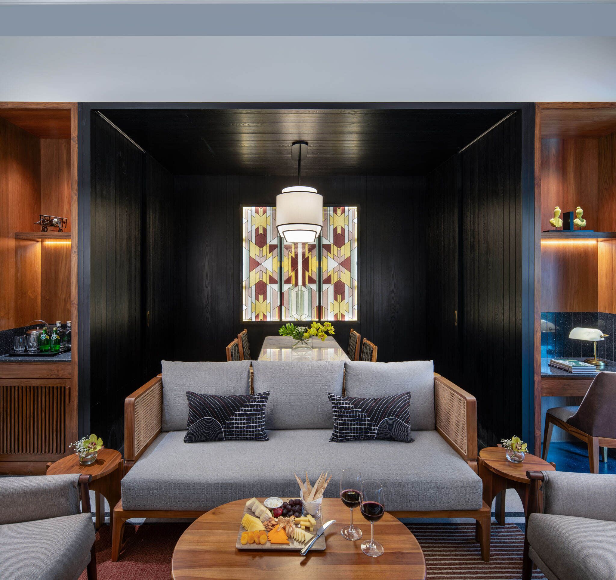 A modern living room with a sofa, two side tables, a coffee table with snacks and wine glasses, and a decorative light fixture.
