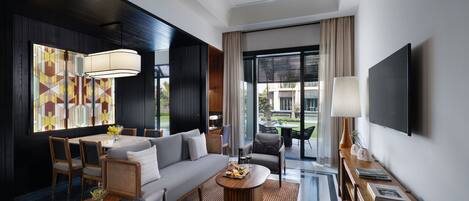 Una habitación de hotel moderna con sofá, sillas, una mesa de comedor, televisor y un ventanal con vistas.