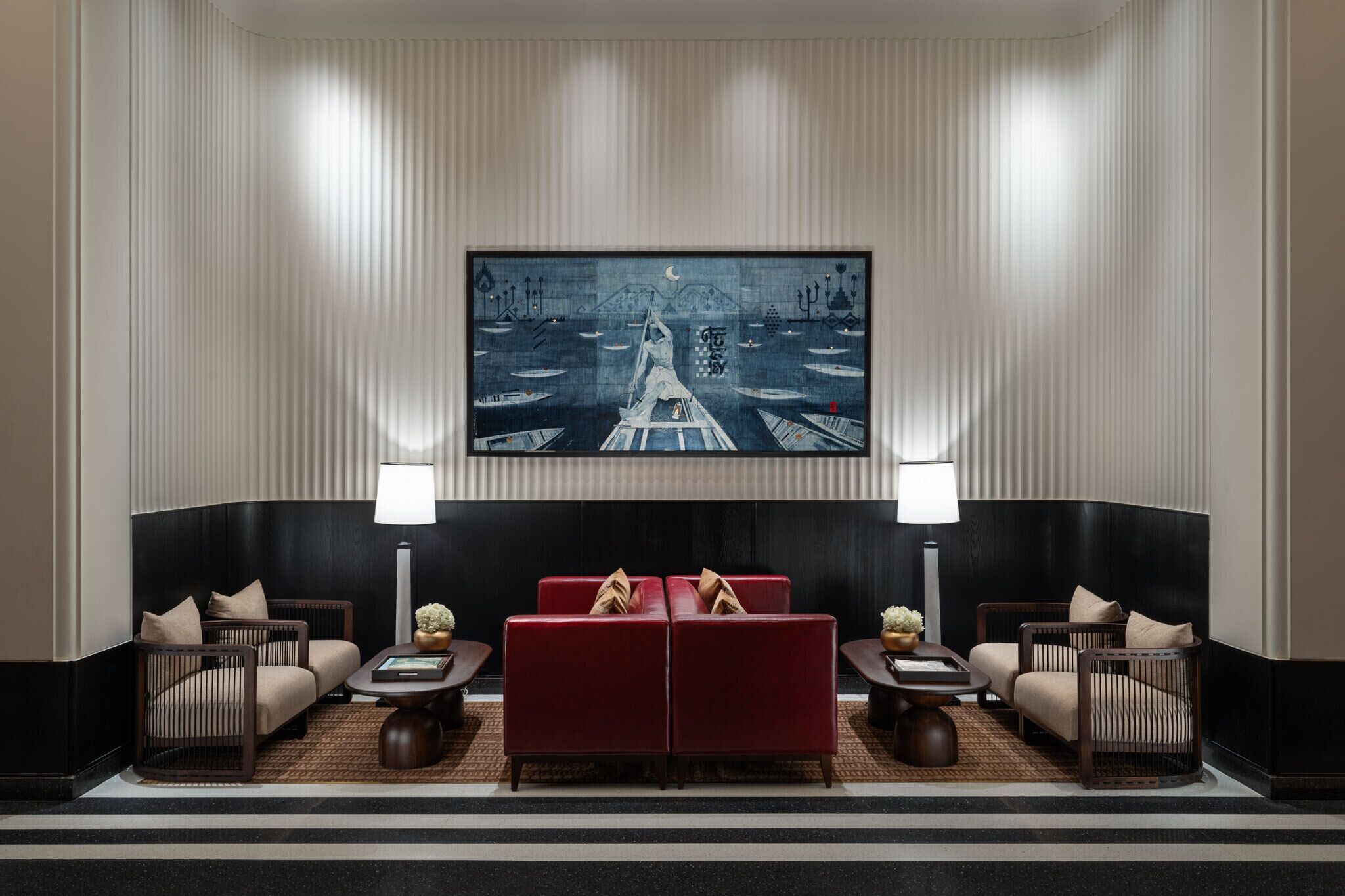 Una hall d'albergo con un grande quadro che raffigura una scena fluviale, due divani rossi e un divisorio nero.
