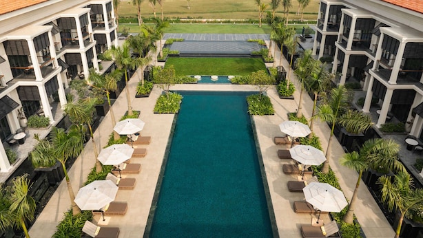 Zona de piscina con sillones de descanso y sombrillas, rodeada de edificios con balcones y vistas a una masa de agua.