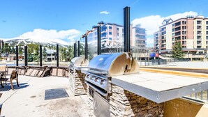 An outdoor patio with a stone barbecue grill, outdoor seating, and a view of a mountain in the background. - Resort 1 Bedroom/2 Bathroom at Peak 9 Base/Main St (Breckenridge)