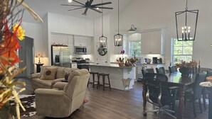 A modern kitchen with white cabinets, a central island, and a dining area with a table and chairs. - Cottage near Elijah State Park, Savannah Lakes Village, Baker and Hickory Knob. (Lincolnton)