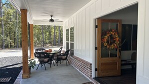 A covered patio with a table and chairs, a wooden door with a wreath, and a brick wall. - Cottage near Elijah State Park, Savannah Lakes Village, Baker and Hickory Knob. (Lincolnton)